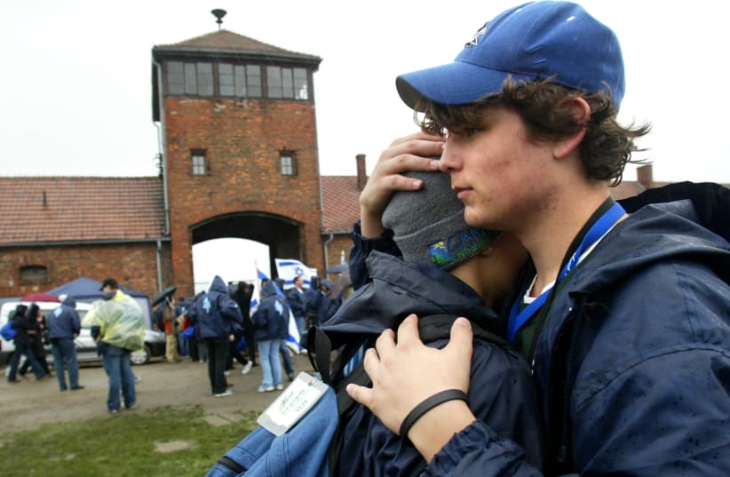Two boys hug in front of the main railway building of the former Nazi death camp Birkenau (Auschwitz II) during the 'March of the Living' in Oswiecim, Poland (photo credit: KATARINA STOLTZ/ REUTERS)