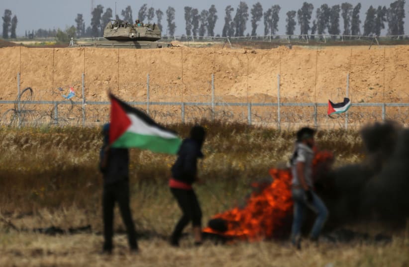 Israel soldiers ride on a military vehicle as Palestinian demonstrators are seen during clashes at a tent city protest at Israel-Gaza border, in the southern Gaza Strip (photo credit: IBRAHEEM ABU MUSTAFA/REUTERS)