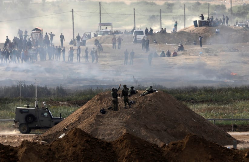 Israeli soldiers are seen next to the border fence on the Israeli side of the Israel-Gaza border, as Palestinians protest on the Gaza side of the border, Israel April 5, 2018. (photo credit: AMIR COHEN/REUTERS)