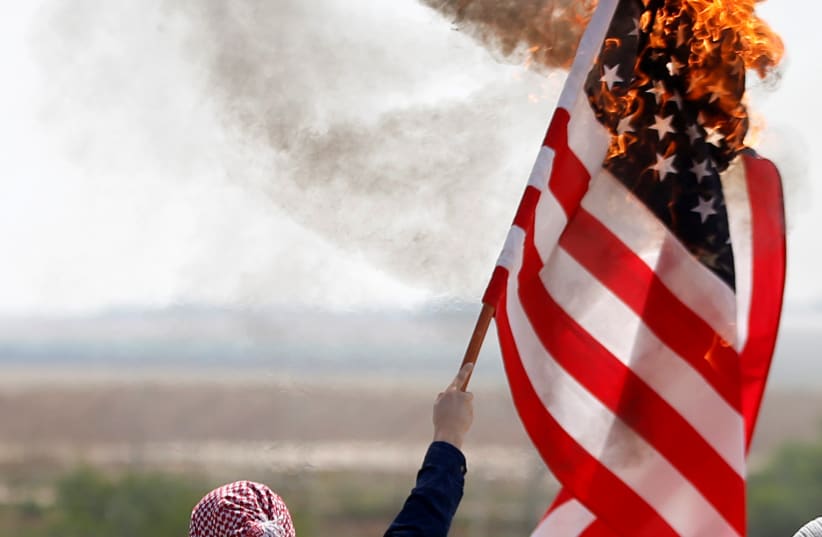 A Palestinian burns an American flag during protests in Gaza (photo credit: MOHAMMED SALEM/ REUTERS)