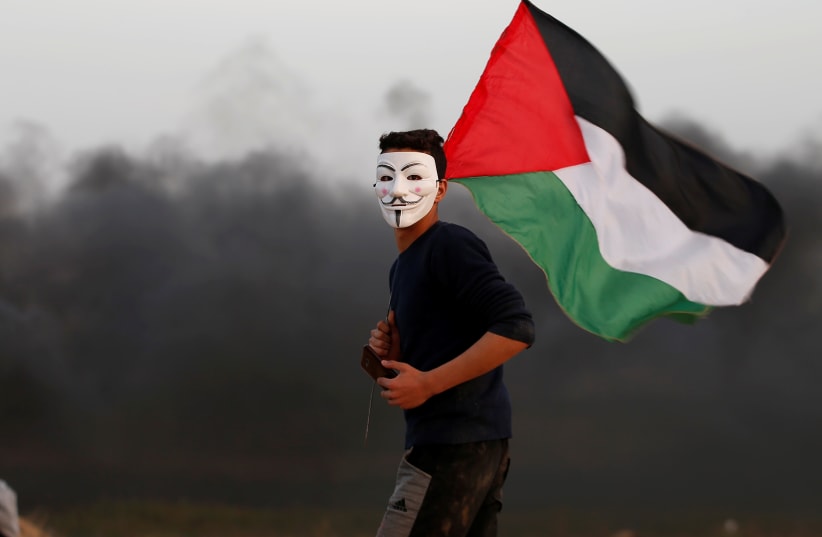 A Palestinian wears an 'Anonymous' mask and holds a Palestinian flag during protests in Gaza (photo credit: MOHAMMED SALEM/ REUTERS)