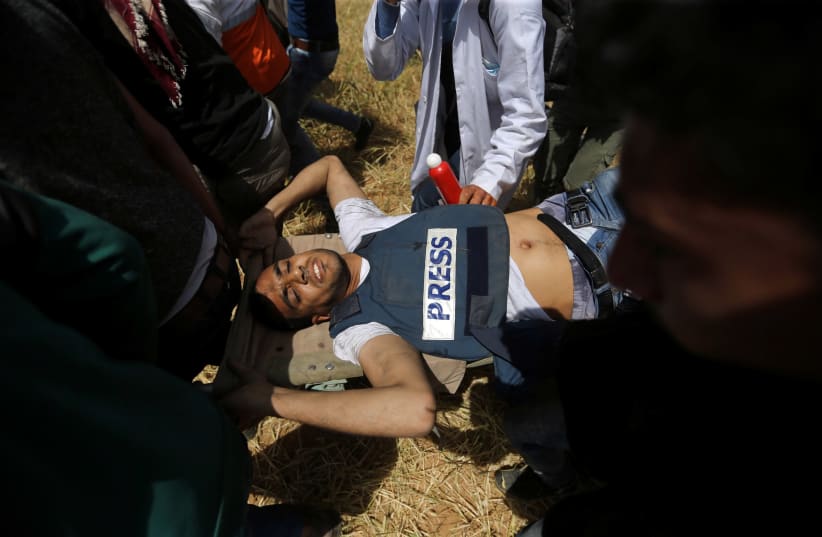 Mortally wounded Palestinian journalist Yasser Murtaja, 31, is evacuated during clashes with Israeli troops at the Israel-Gaza border, in the southern Gaza Strip April 6, 2018. (photo credit: IBRAHEEM ABU MUSTAFA / REUTERS)