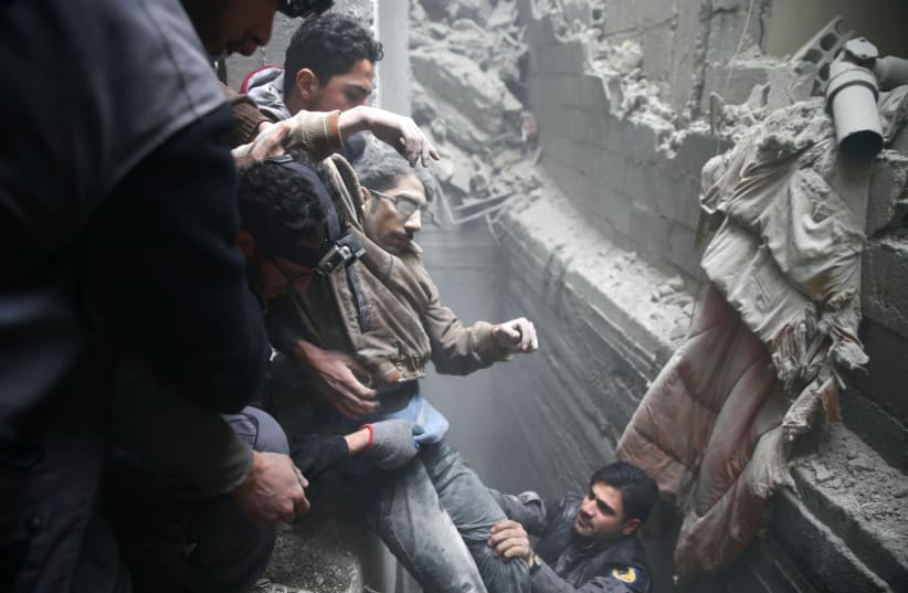 Civil defense help a man from a shelter in the besieged town of Douma in eastern Ghouta in Damascus, Syria, February 22, 2018. (photo credit: REUTERS/BASSAM KHABIEH)