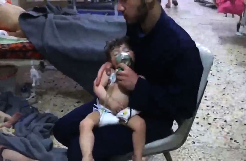 An image grab from a video released by the Syrian civil defence in Douma shows an unidentified volunteer holding an oxygen mask over a child's face at a hospital following a reported chemical attack on the rebel-held town on April 8, 2018 (photo credit: HO / AFP / SYRIA CIVIL DEFENCE)
