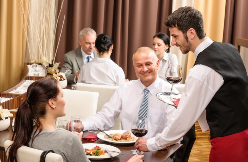 A waiter serves people at a restaurant (photo credit: INGIMAGE)