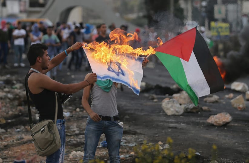 A Palestinian protester burns a replica Israeli flag as another holds a Palestinian flag during clashes with the Israeli troops near the Jewish settlement of Bet El, near the West Bank city of Ramallah October 18, 2015. (photo credit: MOHAMAD TOROKMAN/REUTERS)