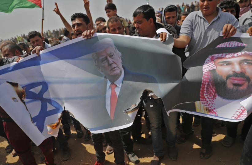 Palestinians prepare to set fire on an Israeli flag and portraits of US President Donald Trump and Saudi Crown Prince Mohammed bin Salman during a protest at the border fence with Israel, east of Khan Yunis in the southern Gaza city, on April 13, 2018 (photo credit: THOMAS COEX / AFP)