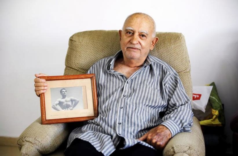 Aharon Ben Hur, 84, who immigrated from Iraq to Israel in 1951, holds an old photo of himself in his house in Rehovot, Israel, April 16, 2018. Picture taken April 16, 2018. (photo credit: AMIR COHEN/REUTERS)