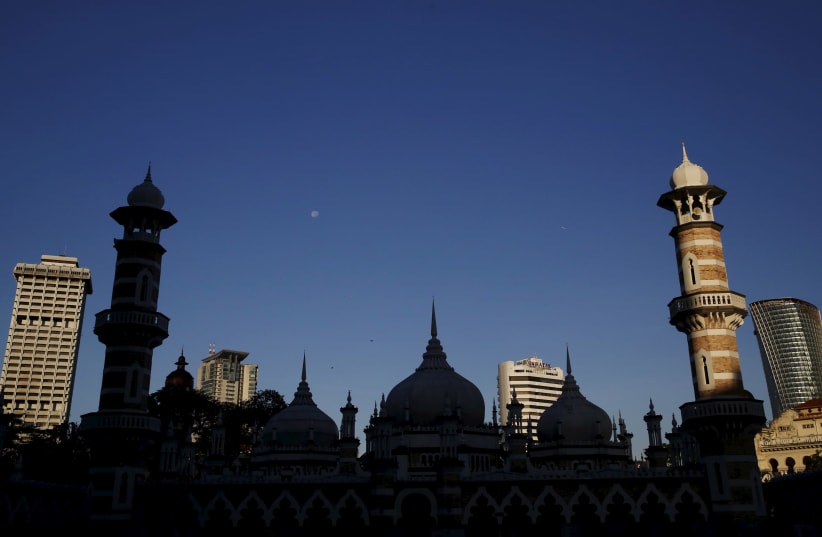 A mosque is silhouetted against city buildings in Kuala Lumpur, Malaysia, January 27, 2016. (photo credit: OLIVIA HARRIS/ REUTERS)