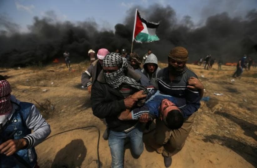 A wounded demonstrator is evacuated during clashes with Israeli troops at a protest at the Israel-Gaza border in the southern Gaza Strip, April 27, 2018 (photo credit: IBRAHEEM ABU MUSTAFA / REUTERS)