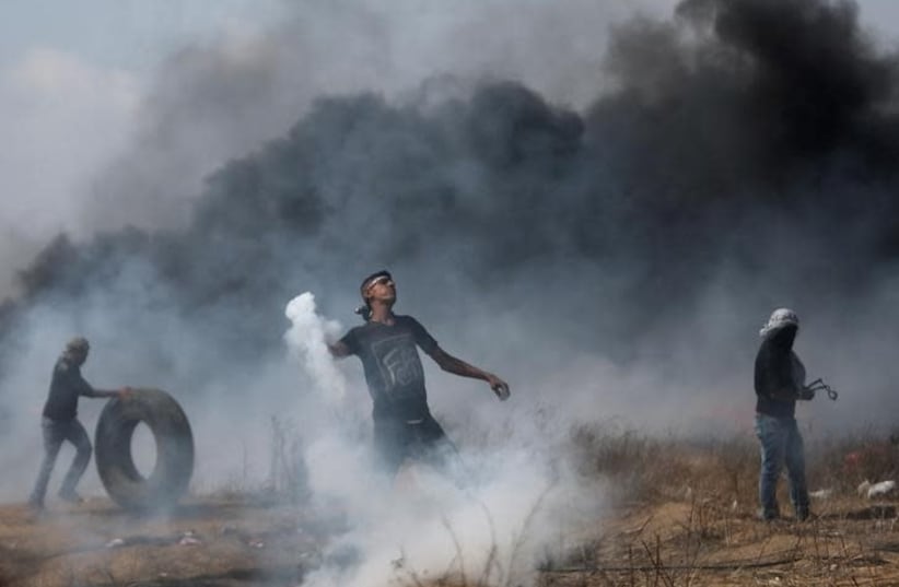 A demonstrator hurls back a tear gas canister fired by Israeli troops during clashes at a Gaza border protest , April 27, 2018 (photo credit: REUTERS/IBRAHEEM ABU MUSTAFA)