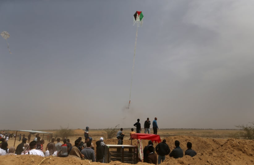 Palestinians set a kite on fire to be thrown at the Israeli side during clashes at a protest at the Israel-Gaza border in the southern Gaza Strip, April 20, 2018 (photo credit: IBRAHEEM ABU MUSTAFA / REUTERS)