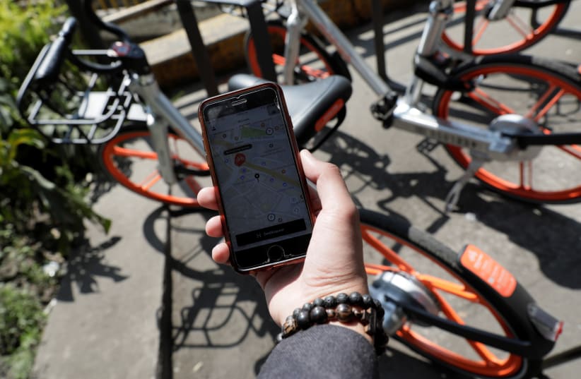 A man holds his mobile phone displaying the Mobike app next to a parked bicycle (photo credit: HENRY ROMERO / REUTERS)