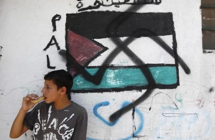 A Palestinian boy stands next to a Palestinian flag with a swastika painted over it as protesters march in solidarity with Palestinians against a Jewish settlement in the Sheikh Jarrah neighbourhood of East Jerusalem July 17, 2010 (photo credit: BAZ RATNER/REUTERS)
