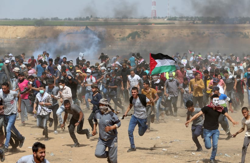 Palestinian demonstrators run for cover from tear gas fired by Israeli forces during a protest at the Israel-Gaza border in the southern Gaza Strip, May 11, 2018 (photo credit: REUTERS/IBRAHEEM ABU MUSTAFA)