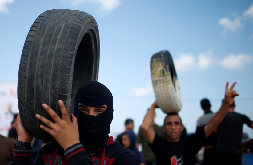 Palestinian demonstrators carry tires during a protest against U.S. embassy move to Jerusalem and ahead of the 70th anniversary of Nakba, at the Israel-Gaza border, east of Gaza City May 14, 2018. (photo credit: REUTERS/MOHAMMED SALEM)