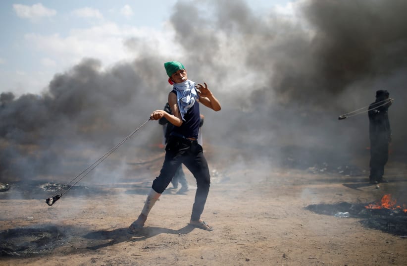 A Palestinian demonstrator uses a sling to hurl stones at Israeli troops during a protest at the Israel-Gaza border east of Gaza City May 14, 2018 (photo credit: REUTERS/MOHAMMED SALEM)