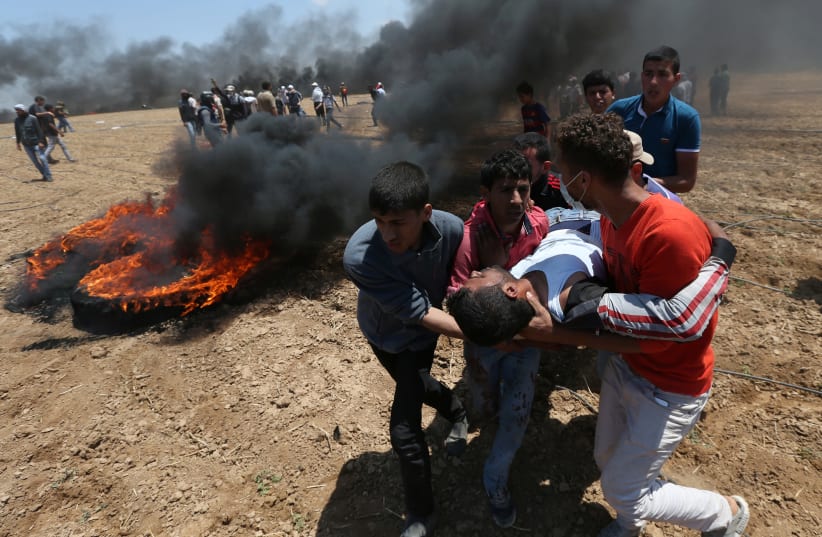 A wounded Palestinian is evacuated during a protest at the Israel-Gaza border in the southern Gaza Strip May 14, 2018 (photo credit: REUTERS/IBRAHEEM ABU MUSTAFA)