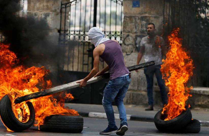 A Palestinian demonstrator moves a burning tire during a protest in Bethlehem in the West Bank May 14, 2018. (photo credit: REUTERS/MUSSA QAWASMA)