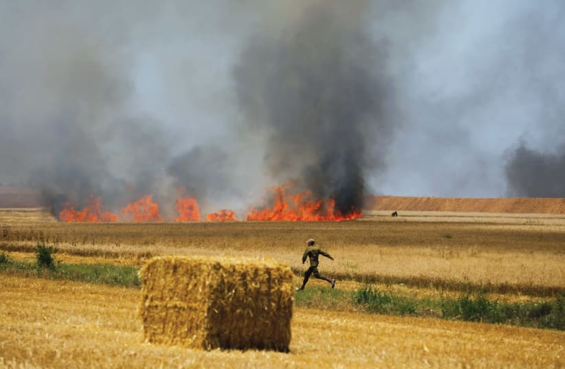 AN IDF soldier runs in a field near Kibbutz Mefalsim, which was set on fire by Palestinians in Gaza on May 14 (photo credit: REUTERS/AMIR COHEN)