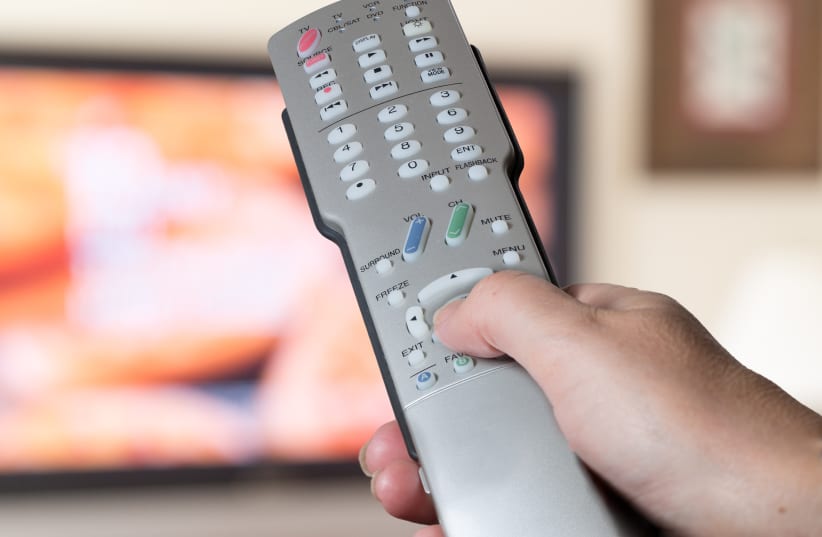 Silver television remote control being pressed by thumb with out of focus screen background (Illustrative) (photo credit: INGIMAGE)
