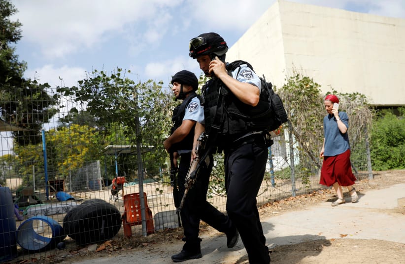 Israeli policemen walk past a kindergarten yard damaged by mortar shells fired from the Gaza Strip in a Kibbutz on the Israeli side of the Israeli-Gaza border, May 29, 2018. (photo credit: REUTERS/AMIR COHEN)