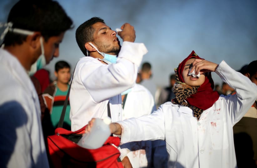 Female Palestinian medic Razan Al-Najar reacts to tear gas as she works at the scene of clashes at Israel-Gaza border, in the southern Gaza Strip, April 1, 2018 (photo credit: IBRAHEEM ABU MUSTAFA / REUTERS)