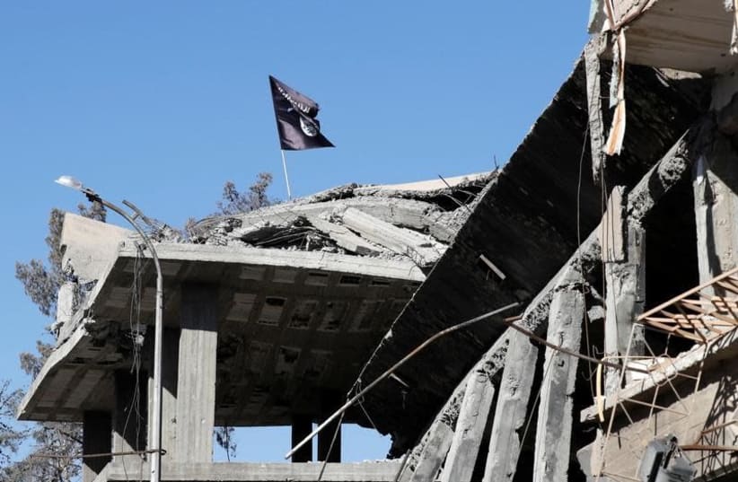 A flag of Islamic State militants is pictured above a destroyed house near the Clock Square in Raqqa, Syria October 18, 2017. Picture taken October 18, 2017. (photo credit: REUTERS/ERIK DE CASTRO)