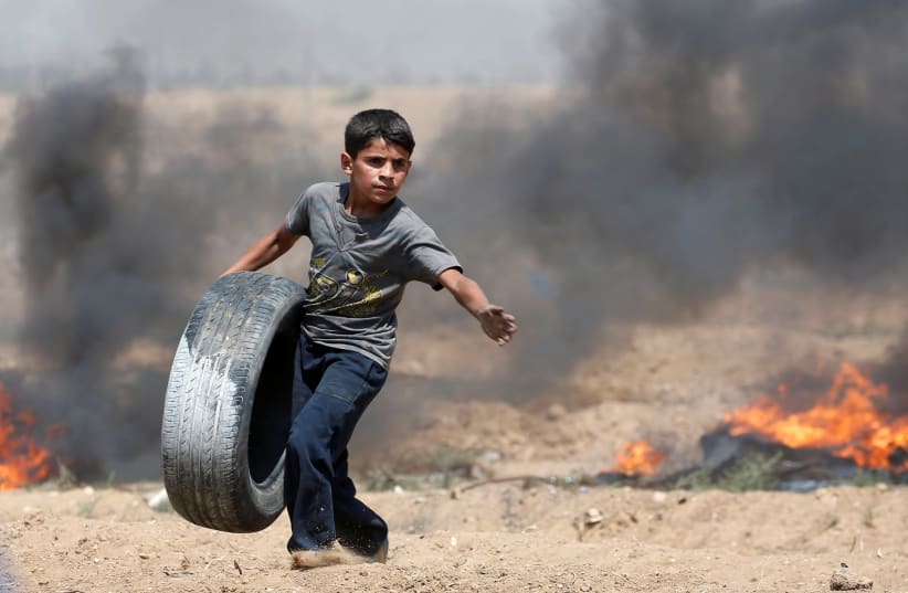 A Palestinian boy carries a tire during a protest marking al-Quds Day, (Jerusalem Day), at the Israel-Gaza border, east of Gaza City June 8, 2018. (photo credit: MOHAMMED SALEM/ REUTERS)