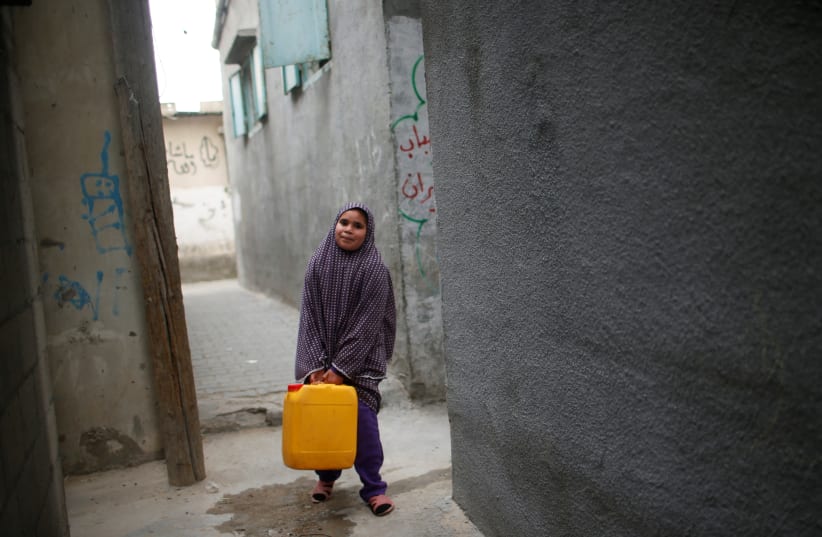 A Palestinian girl carries a potable water container after filling it from a public tap in Jabaliya refugee camp in the northern Gaza Strip (photo credit: MOHAMMED SALEM/REUTERS)