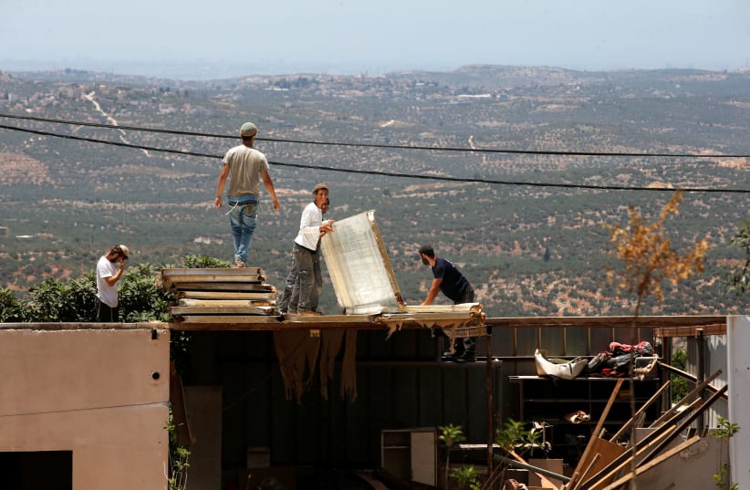 Jewish settlers dismantle parts of a structure during the eviction of buildings that an Israeli court deemed to have been built illegally in the Tapuach West outpost, in the West Bank, June 17, 2018. (photo credit: RONEN ZVULUN/ REURERS)