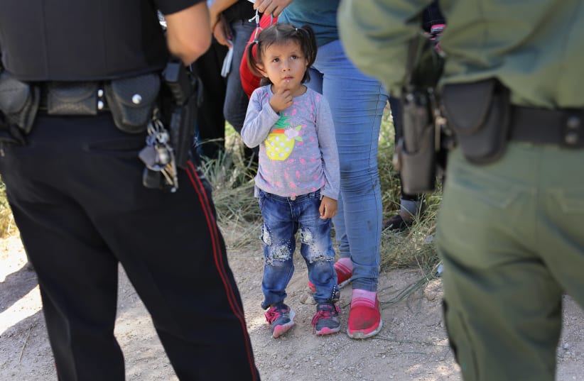 A Mission Police Dept. officer (L), and a US Border Patrol agent watch over a group of Central American asylum seekers before taking them into custody on June 12, 2018 near McAllen, Texas (photo credit: JOHN MOORE/GETTY IMAGES/AFP)