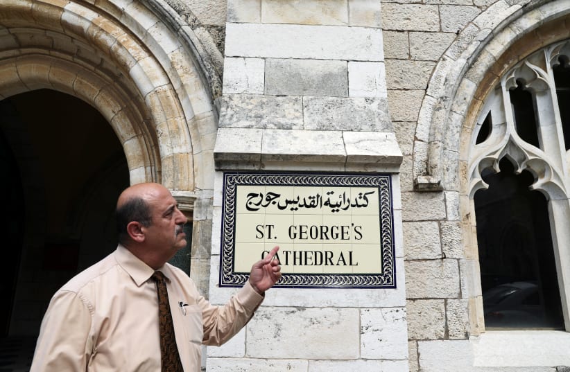 A church official gestures as he stands next to the entrance to the Anglican St. George's Cathedral in Jerusalem, June 13, 2018 (photo credit: REUTERS/AMMAR AWAD)