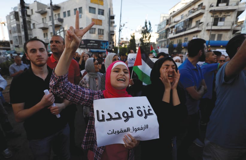 A Palestinian protester holds up a sign that reads 'Gaza unites us,' during a demonstration in Ramallah calling on Palestinian Authority President Mahmoud Abbas to lift sanctions on the Gaza Strip (photo credit: REUTERS)