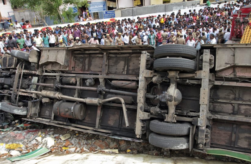 Onlookers stand next to an overturned passenger bus at the site of an accident in the southern Indian city of Chennai June 27, 2012. More than 30 passengers of a Metropolitan Transport Corporation bus were injured after the bus overturned and fell off a flyover, local media reported on Wednesday.  (photo credit: REUTERS)