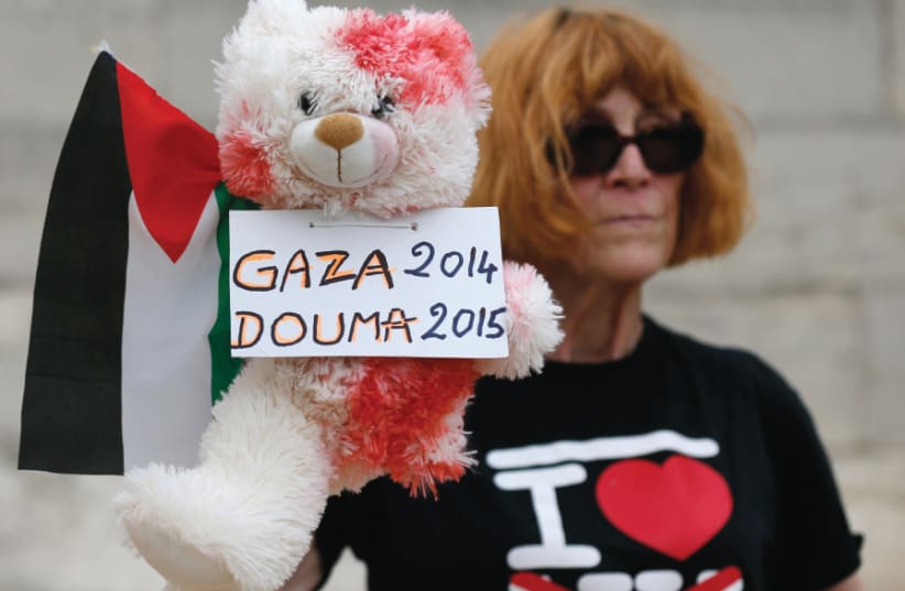 A WOMAN holds a stuffed bear, covered in fake blood, and a Palestinian flag to protest the ‘Tel Aviv on Seine’ event on an artificial sand beach in Paris on August 13, 2015. Leftist critics branded the event ‘indecent’ following an arson attack on a Palestinian family’s home in the West Bank villag (photo credit: REUTERS)