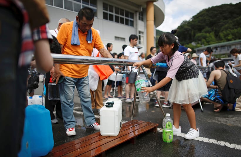 Local residents receive emergency water supply near a flooded area at Mihara Daini junior high school, Japan, July 9, 2018. (photo credit: REUTERS/ISSEI KATO)