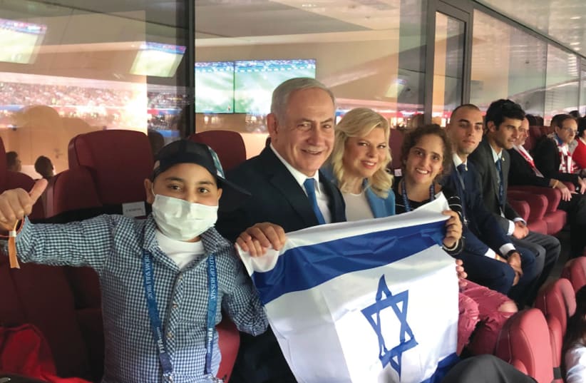 Prime Minister Benjamin Netanyahu and his wife, Sara, proudly display Israel’s flag at the World Cup semifinal game between England and Croatia in Moscow on Wednesday, flanked by cancer patients Alon Eizarayev, 13 (left), and Mika Lipsker, 18, who went with them to Russia July 12, 2018 (photo credit: Courtesy)