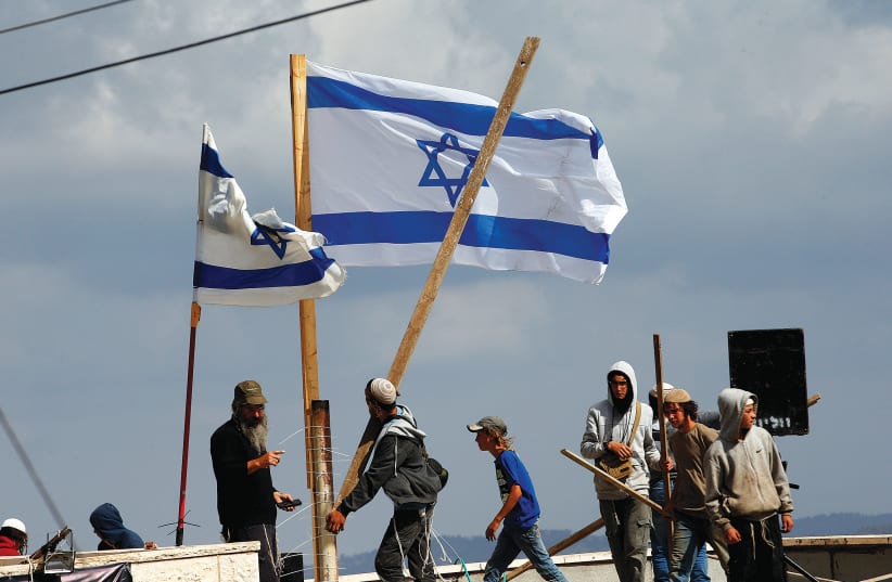 PROTESTERS CARRY wooden sticks as they stand on a roof during the evacuation of families from the illegal outpost of Netiv Ha’avot last month.  (photo credit: RONEN ZVULUN/REUTERS)