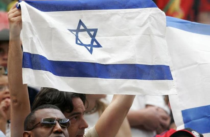 A man holds up an Israeli flag at the start of a soccer match [Illustrative] (photo credit: REUTERS)