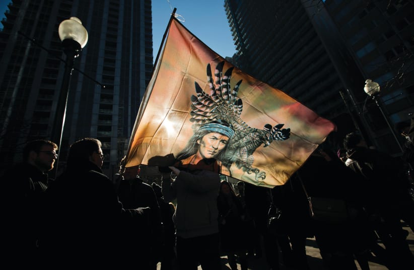 First nations protesters are silhouetted behind a flag as they take part in a demonstration in Toronto in 2013 (photo credit: REUTERS)