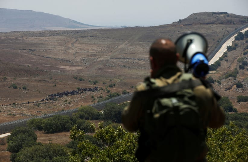An Israeli soldier speaks over a megaphone to people which stand next to the border fence between Israel and Syria from its Syrian side as it is seen from the Golan Heights near the Israeli Syrian border July 17, 2018. (photo credit: RONEN ZVULUN / REUTERS)