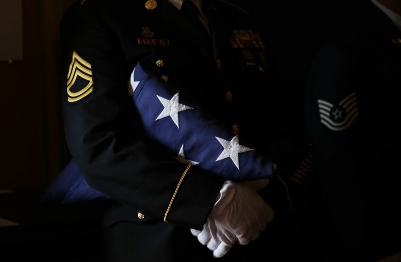 A member of a US military color guard holds a folded American flag during a military funeral (photo credit: KEVIN LAMARQUE/REUTERS)