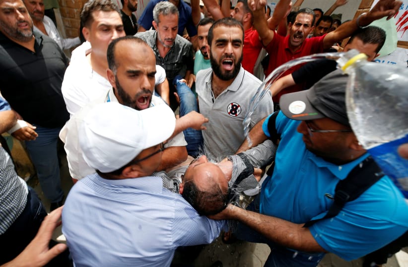 People spray water on a Palestinian UNRWA employee who tried to set himself on fire during a protest against jobs termination by UNRWA inside its headquarters in Gaza City July 25, 2018 (photo credit: MOHAMMED SALEM/ REUTERS)