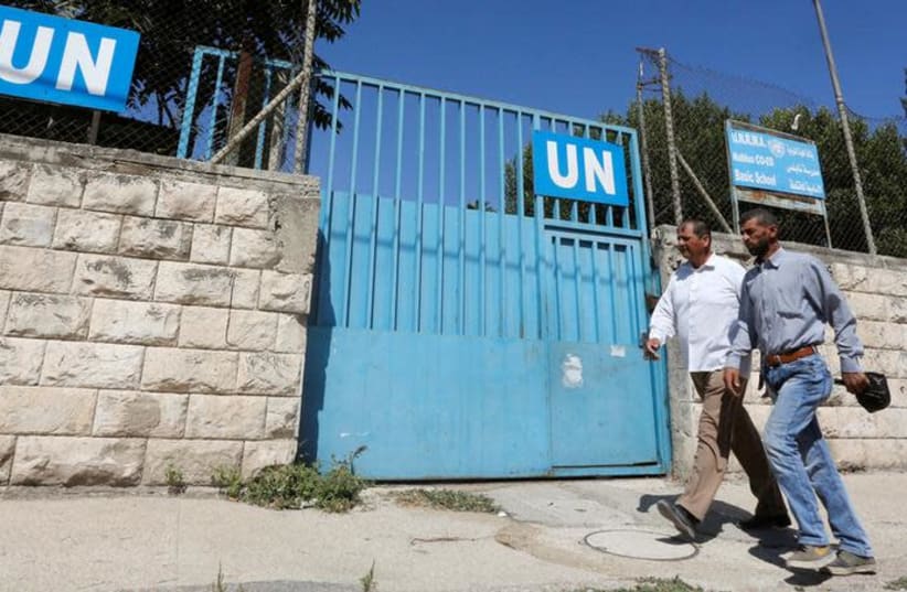 Palestinians pass by the gate of an UNRWA-run school in Nablus in the West Bank August 13, 2018 (photo credit: ABED OMAR QUSINI/REUTERS)