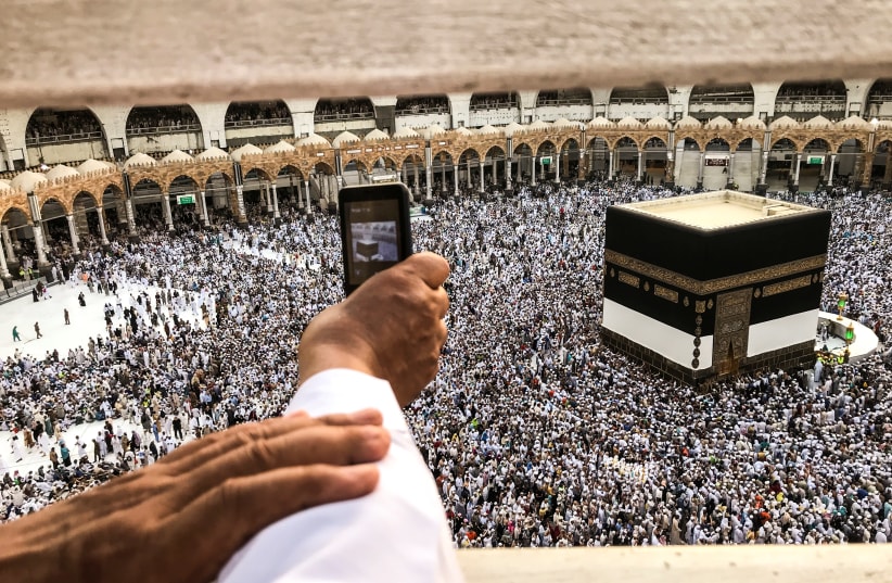 A muslim pilgrim takes a video with his mobile phone while others circle the Kaaba and pray at the Grand mosque ahead of annual Haj pilgrimage in the holy city of Mecca, Saudi Arabia August 16, 2018 (photo credit: ZOHRA BENSEMRA/REUTERS)