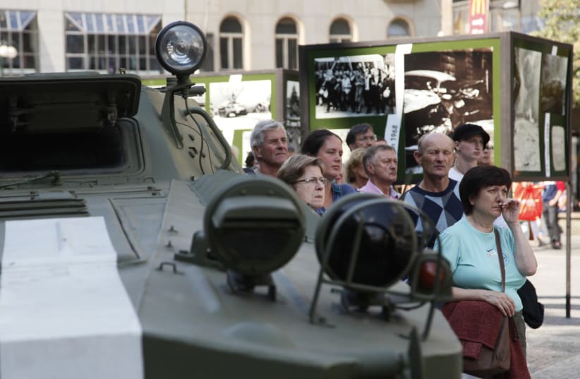 People stand near a Soviet-made military vehicle as they watch a documentary on the Soviet Union-led occupation by the Warsaw Pact armies to halt former Czechoslovak Communist Party leader Alexander Dubcek's Prague Spring political liberalisation reforms in then Czechoslovakia, broadcasted on a disp (photo credit: PETR JOSEK / REUTERS)