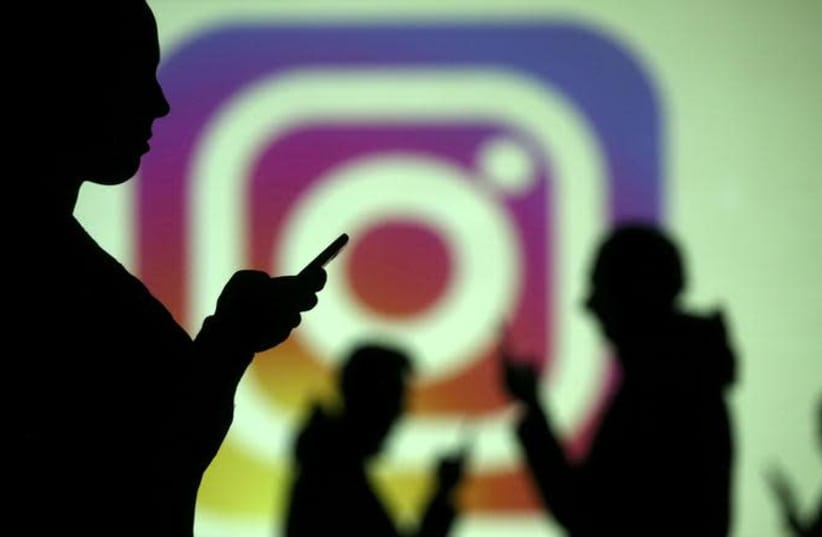 Silhouettes of mobile users are seen next to a screen projection of Instagram logo in this picture illustration taken March 28, 2018 (photo credit: REUTERS/ DADO RUVIC)
