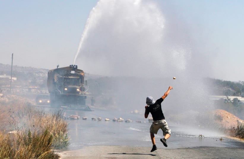 A PALESTINIAN demonstrator hurls a stone as an Israeli truck fires a water cannon during clashes in the West Bank in 2012. (photo credit: REUTERS)