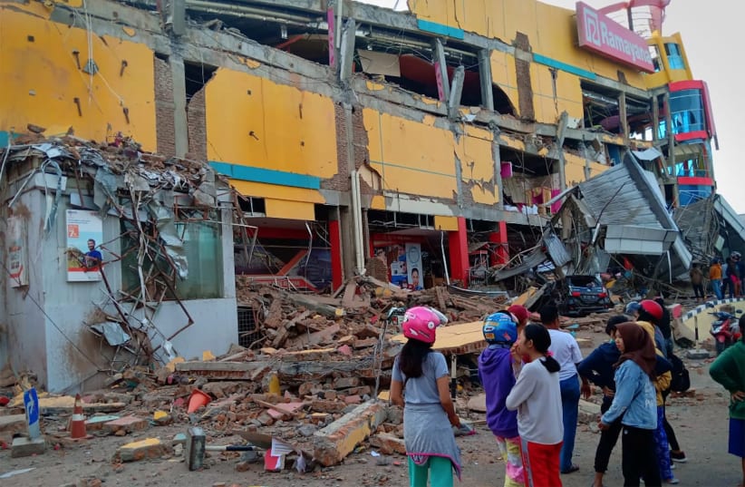 Residents stand in front of a damaged shopping mall after an earthquake hit Palu, Sulawesi Island, Indonesia September 29, 2018. (photo credit: ANTARA FOTO/ROLEX MALAHA VIA REUTERS)